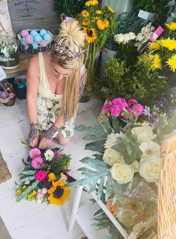 Annie kneeling on the shop floor making up a bright hand-tied bouquet