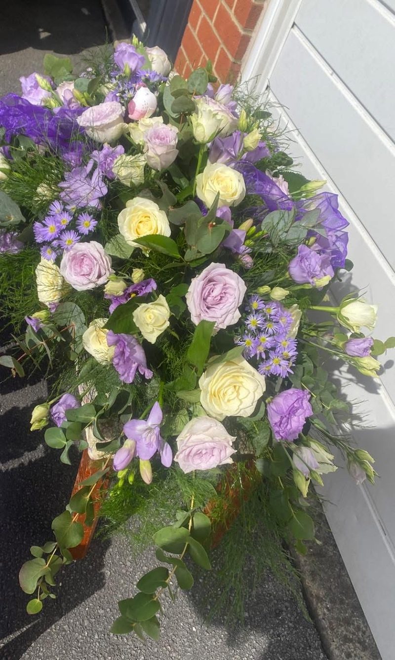 A lilac and ivory casket spray of roses, lisianthus and eucalyptus