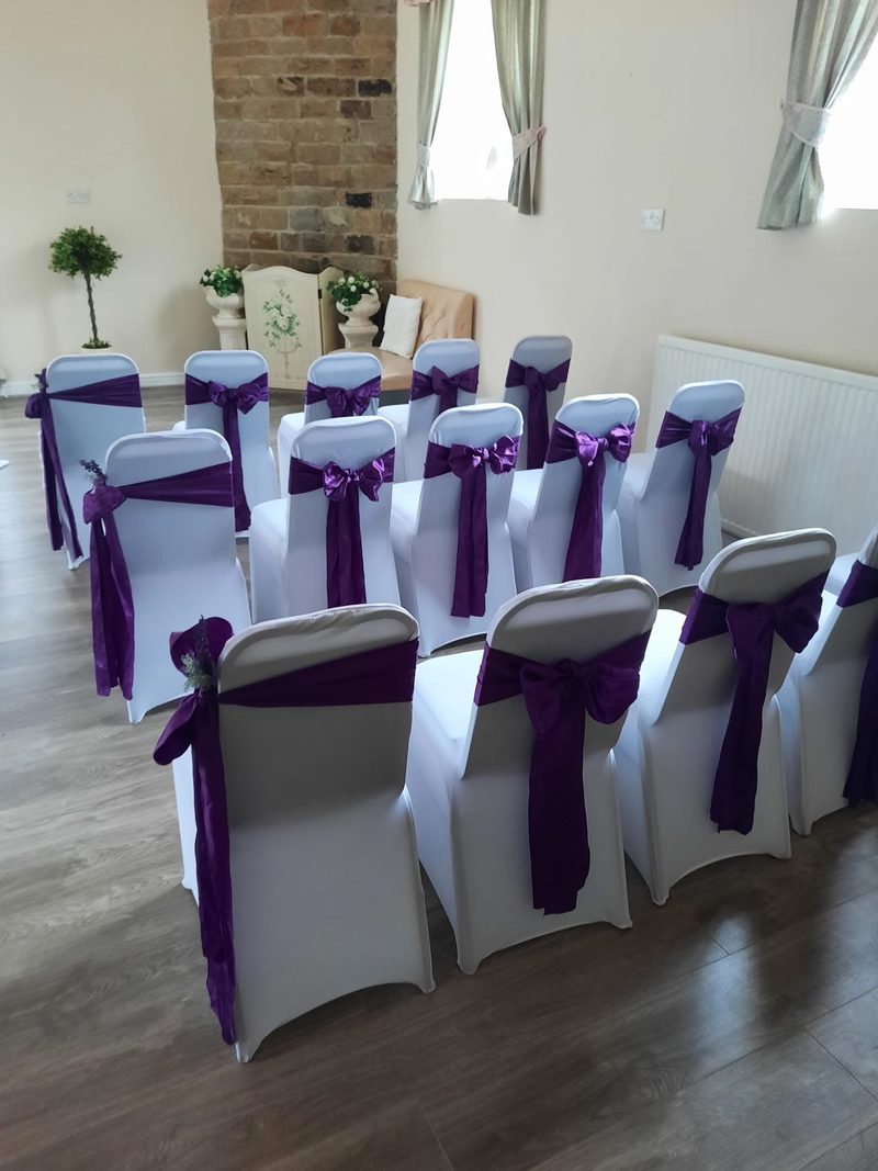 Wedding ceremony chairs dressed with white covers and purple sashes