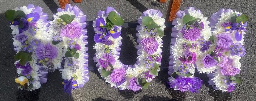 A lettered funeral tribute spelling MUM in white and lilac blooms