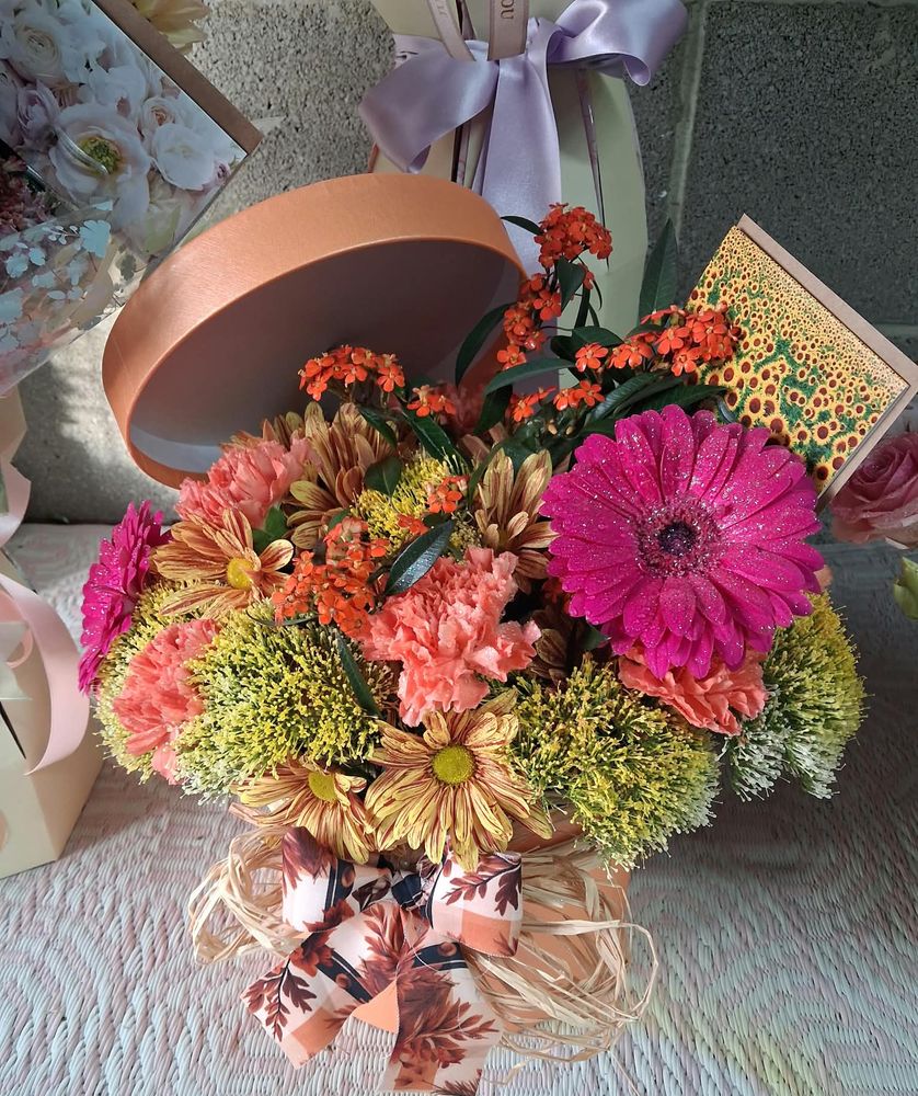 An autumn hat box of coral carnations, bright pink gerberas and orange kalanchoe