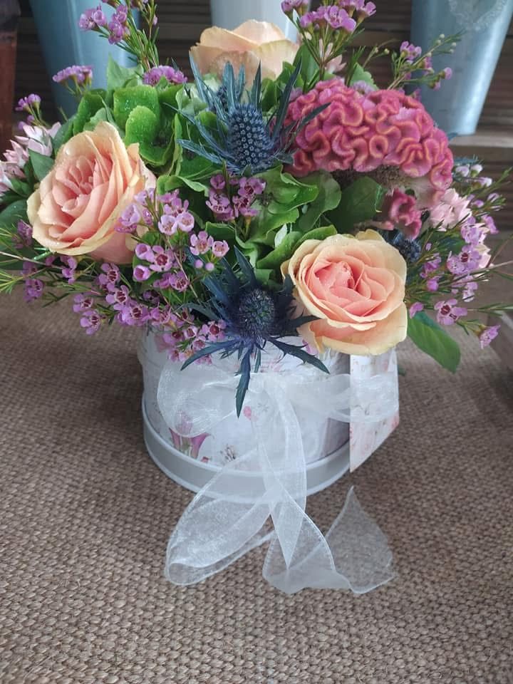 Peach roses, waxflower and thistle in a floral hat box