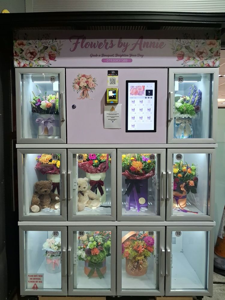 A Flowers by Annie flower machine, its lit compartments filled with boxed bouquets and teddies