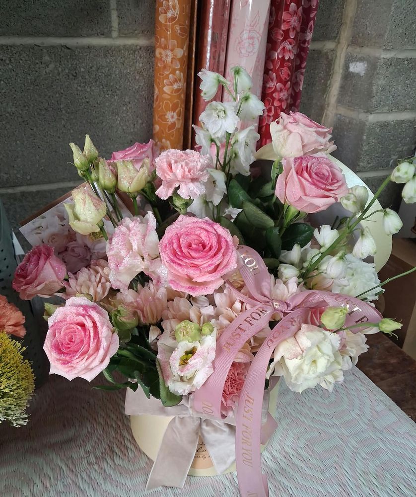 Glittered pink roses, lisianthus and delphinium in a cream hat box with a Just For You ribbon