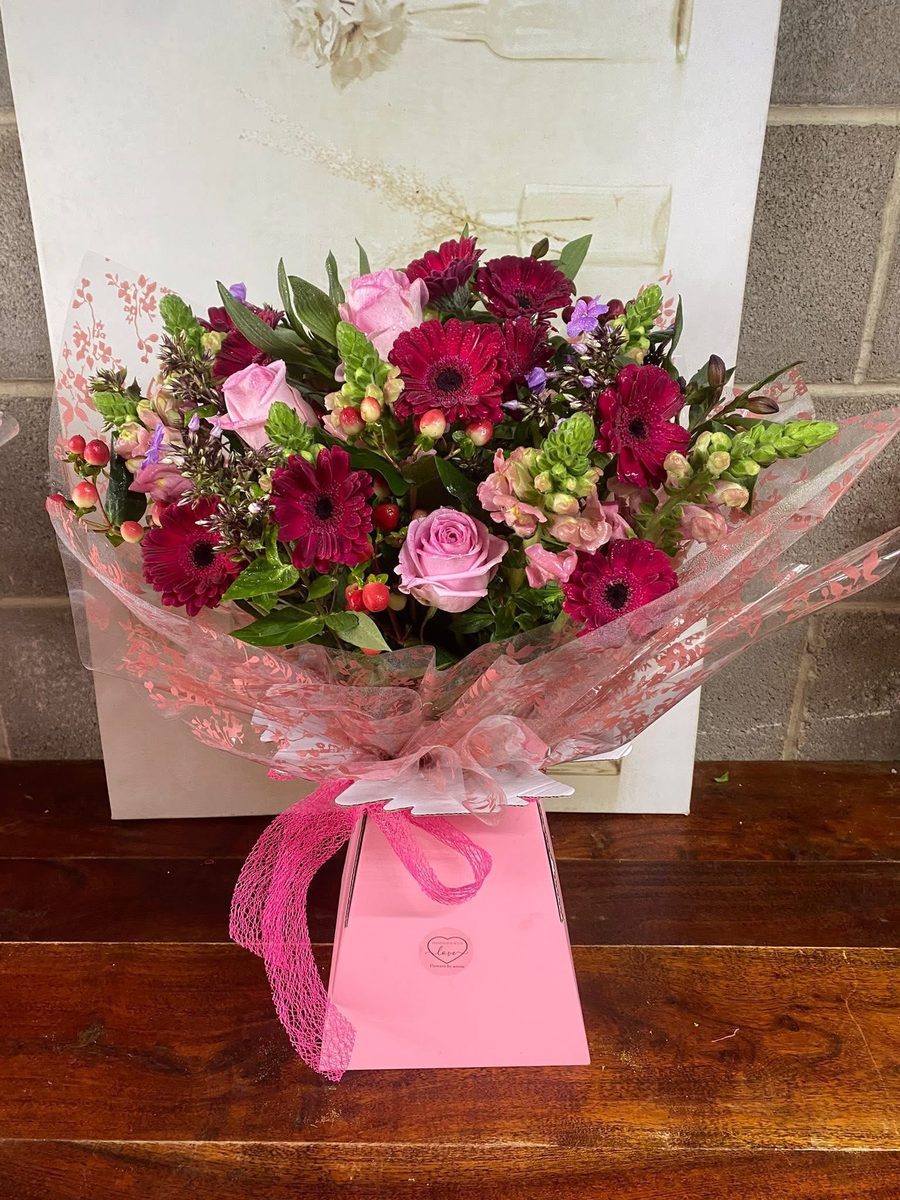 A hand-tied bouquet of pink roses and deep pink gerberas in a Flowers by Annie gift box