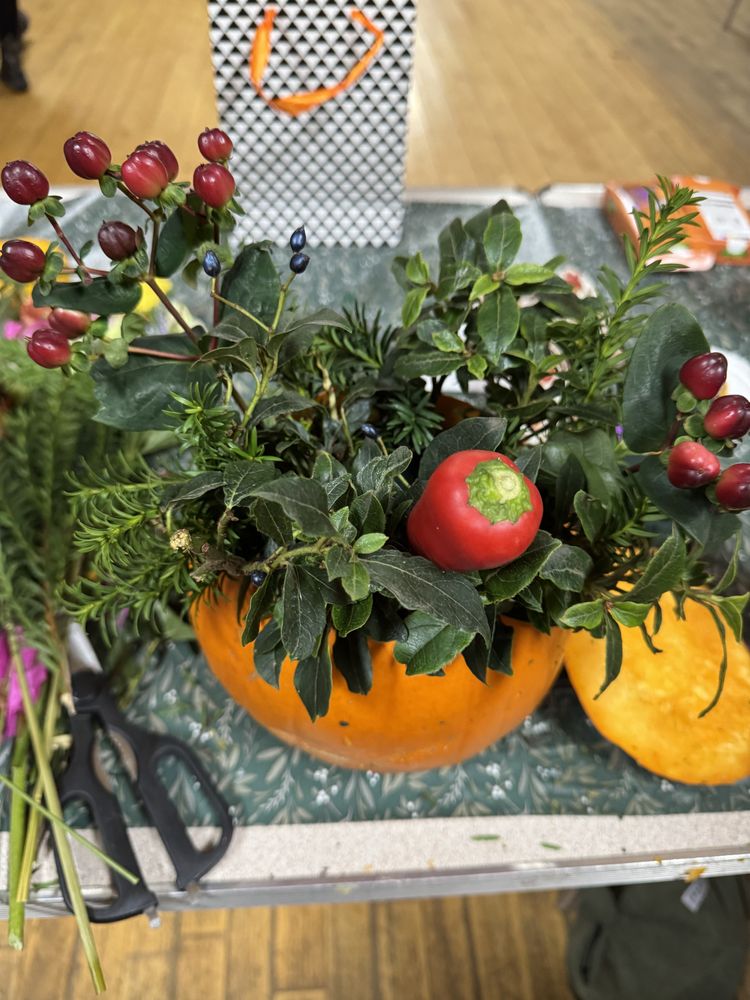 A pumpkin arrangement with berries, foliage and a red pepper